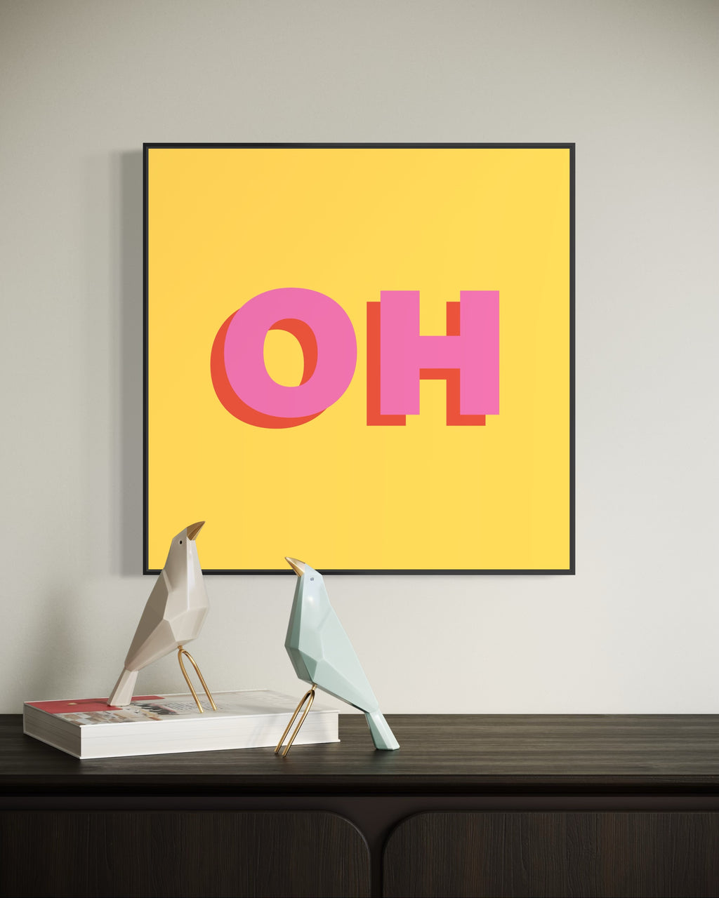 Framed artwork with 'OH' on a yellow background above a desk with decorative items.