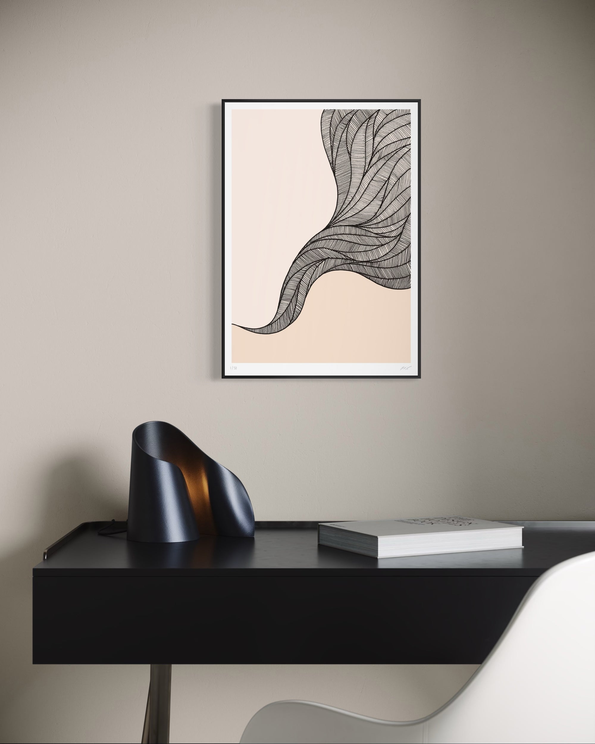 Framed abstract art on a wall above a black desk with a book and decorative object.
