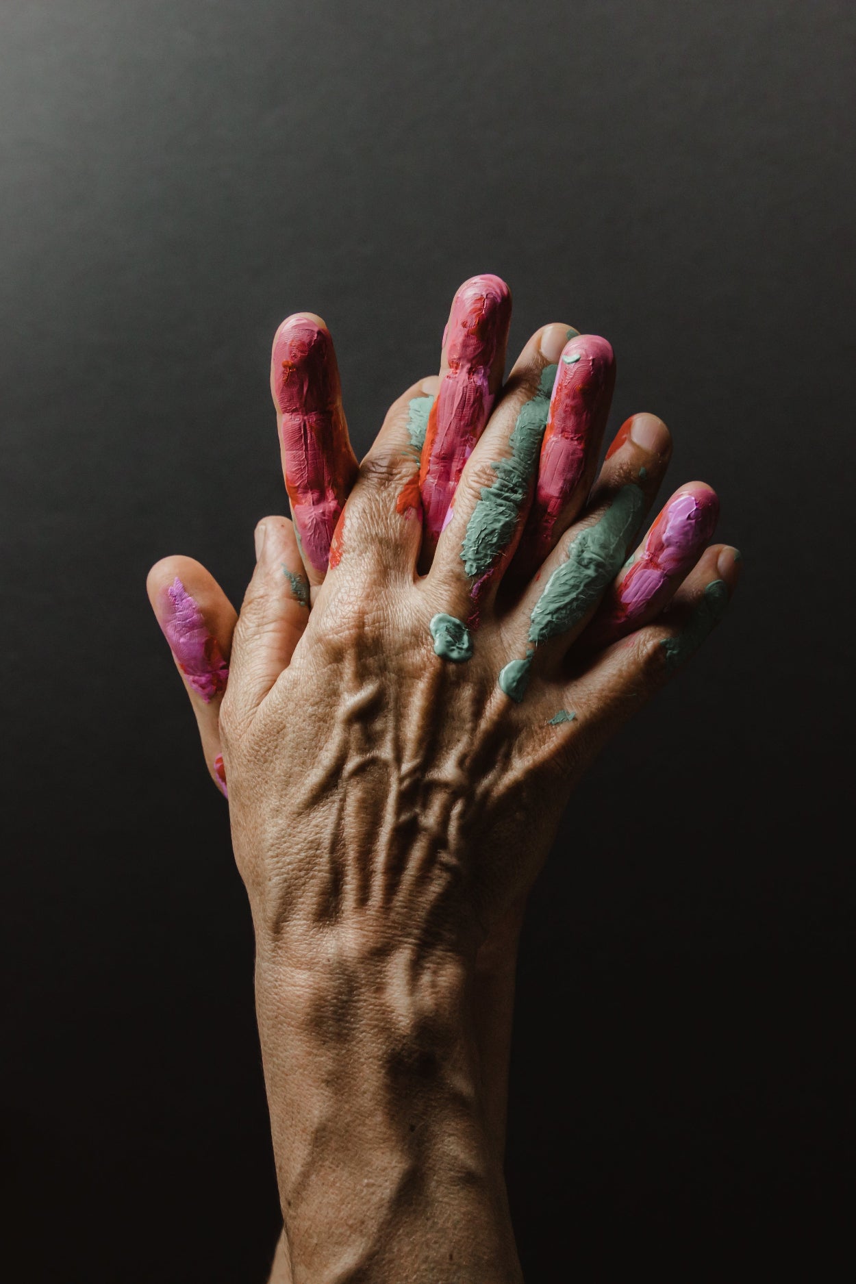 Two hands, palms together, covered in pink and green paint with grey background