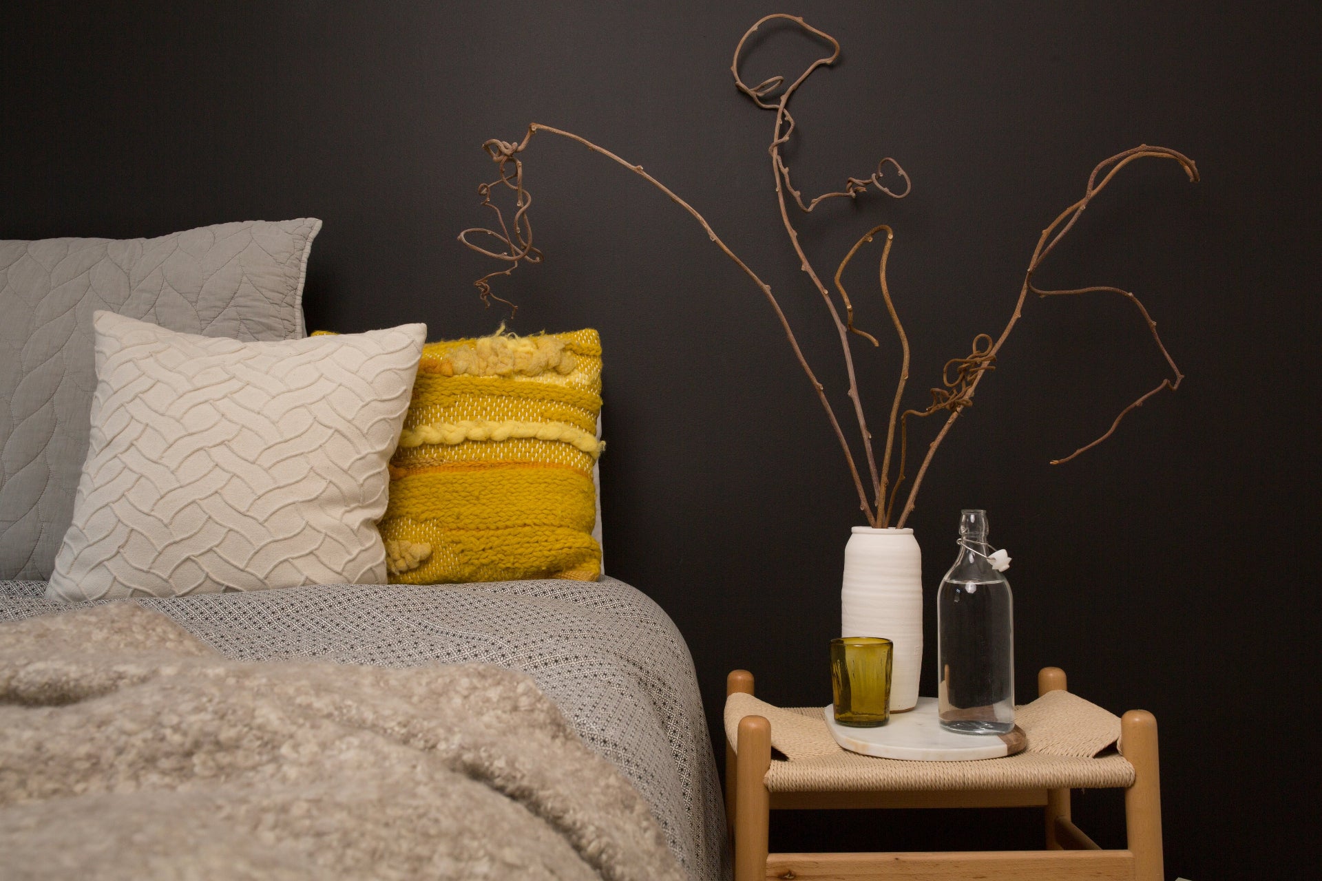 modern bedroom scene with cream and yellow scandi bedding, bedside table and curling twigs in a white vase